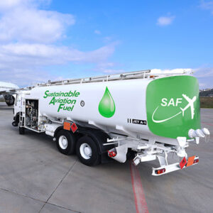 SAF_fe A fuel tanker truck parked on an airport tarmac. This vehicle is clearly marked as carrying sustainable aviation fuel, with the words “Sustainable Aviation Fuel” clearly visible on the side. A green drop symbol accompanies the text, highlighting the fuel’s eco-friendliness. On the rear of the truck, the acronym “SAF” (for Sustainable Aviation Fuel) is displayed alongside a graphic of an airplane. The truck is positioned in a typical airport environment, with an asphalt surface and infrastructure elements visible in the background.